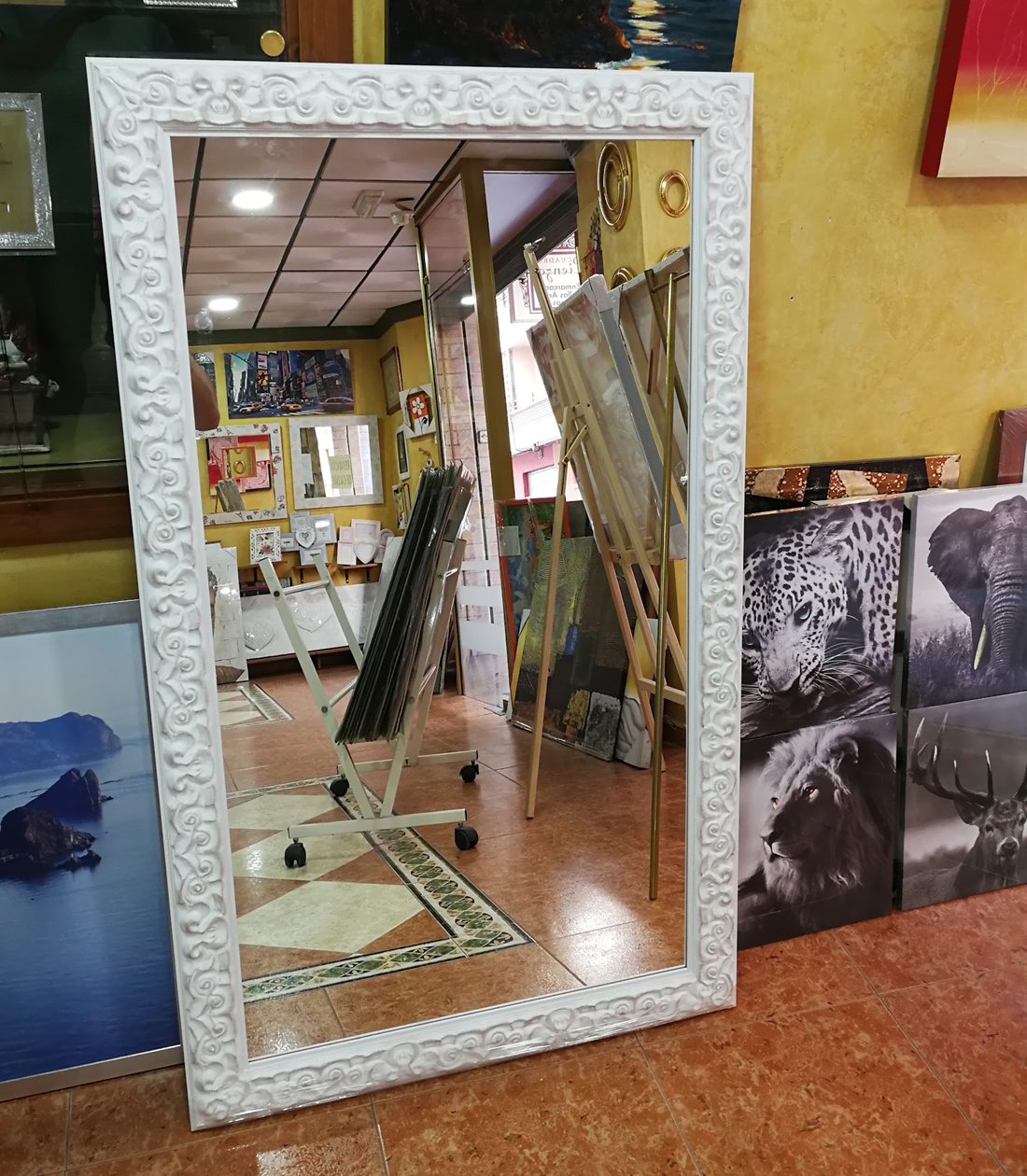 Espejo grande con moldura blanca labrada, apoyado en la tienda.