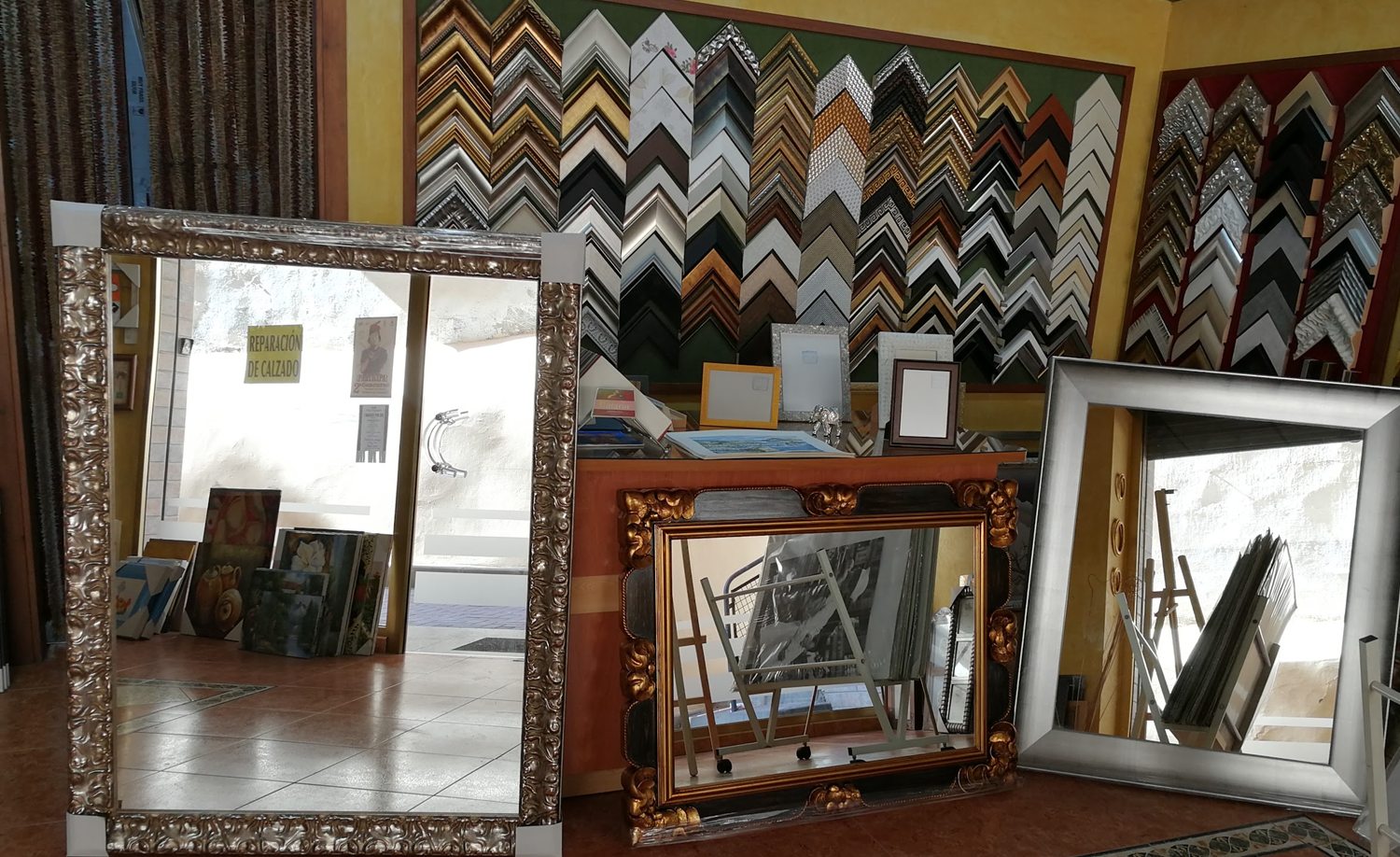 Interior de la tienda con espejos enmarcados en pan de plata y oro delante del muestrario de molduras.